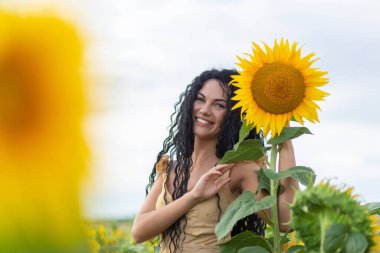 Güzel, gülümseyen, koyu saçlı, elinde bir buket ayçiçeği olan bir kadının portresi.