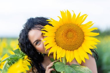 Elinde büyük bir ayçiçeği olan, gülümseyen, siyah saçlı güzel bir kadının portresi.