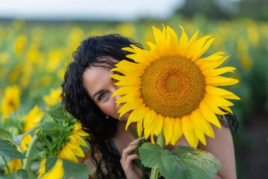 Elinde büyük bir ayçiçeği olan, gülümseyen, siyah saçlı güzel bir kadının portresi.