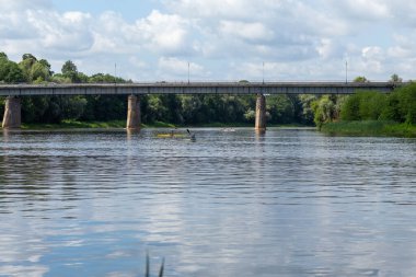 Sporcular bir otomobil köprüsünün arka planına karşı nehirde kano yaparak antrenman yapıyorlar