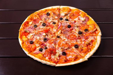 Kızarmış tavuk, domuz pastırması, soğan ve domatesli bir köy pizzası ahşap bir masada kağıt tabakta servis edilir.