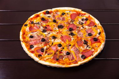Sosisli, pastırmalı, biberli ve mantarlı bütün bir rustik pizza kaprisi ahşap bir masada kağıt tabakta servis edilir.