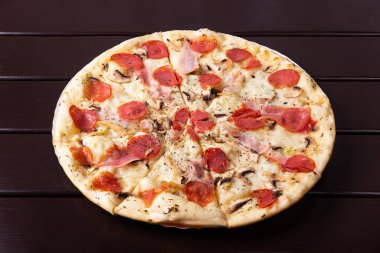 Mozzarella, göğüs eti, mantar ve salamlı bir köy pizzası ahşap bir masada kağıt tabakta servis edilir.
