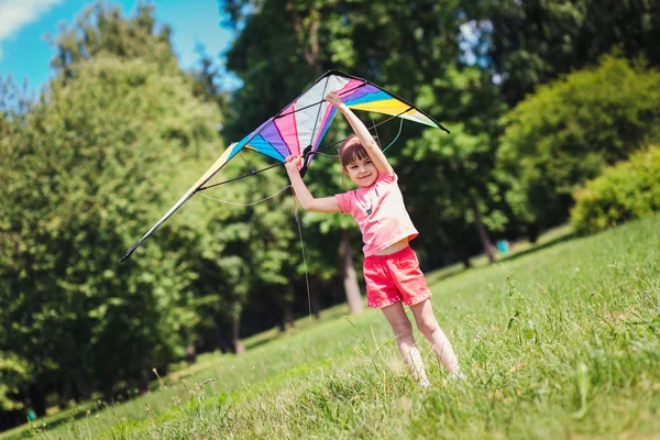Liten flicka spelar med färgad drake i parken. — Stockfoto