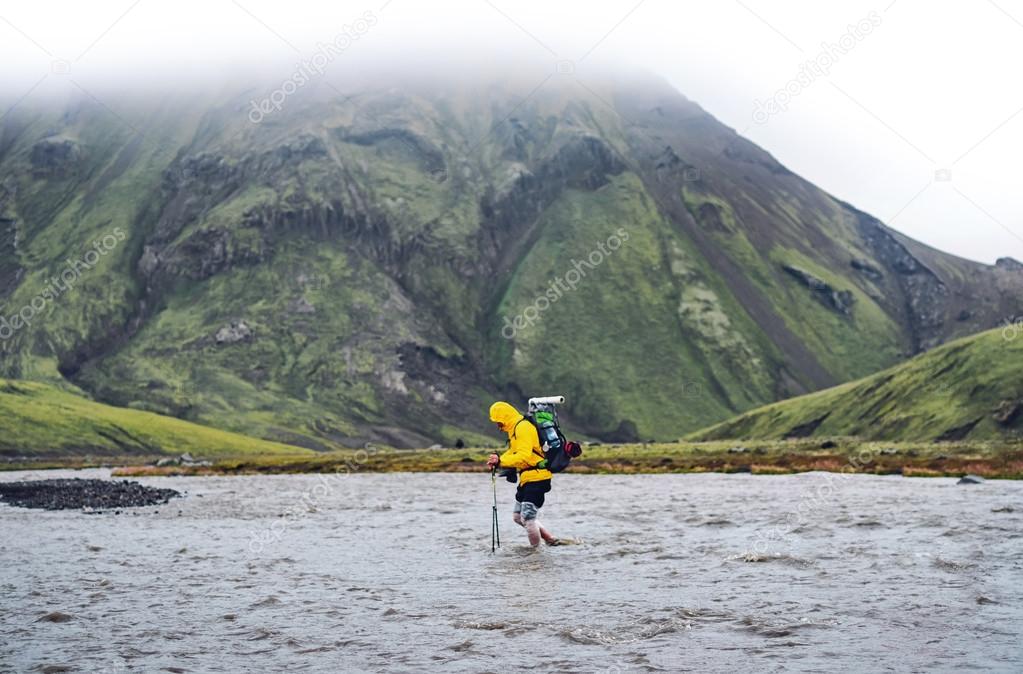 Hiker man with backpack crossing a river in  Iceland. Hiking and leisure theme