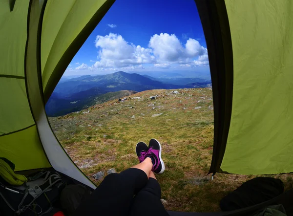 Woman lying in tent with a view of mountain and sky