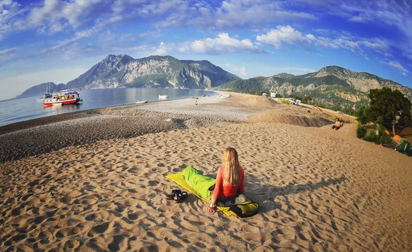 Lycklig kvinna som ligger på stranden, utsikt över bergen, himmel och hav . — Stockfoto