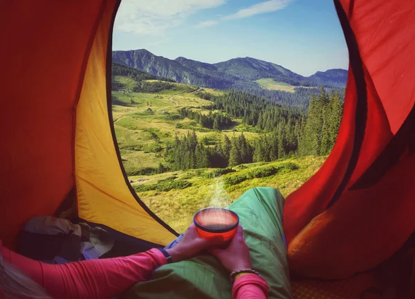 Femme couchée dans une tente avec café, vue sur les montagnes et le ciel — Photo