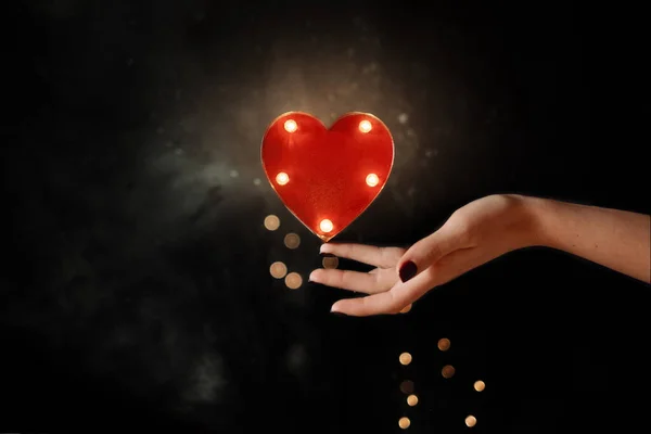 Mujer mano equilibrando el corazón rojo con luz cálida — Foto de Stock