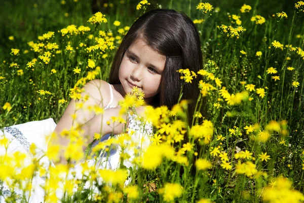 Little girl with dark hair sitting on a field of of yellow flowers on the background — Stock Photo, Image