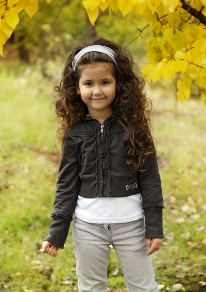 Little cute girl with dark curly hair sitting in the autumn forest — Stock Photo, Image