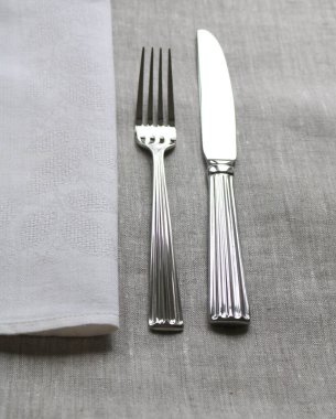 Gri bir masanın üzerinde çatallı ve peçeteli bir bıçak.