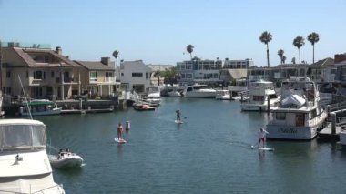 HUNTINGTON BEACH, CA / USA - 16 Temmuz 2019: İnsanlar lüks evler ve yatlar arasında Huntington Limanı 'nda kürek çekiyorlar