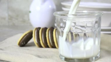 Arka planda kurabiyeler olan bir bardağa süt dökmek