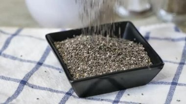 Süper yavaş çekimde bir kaseye siyah chia tohumları dökülüyor.