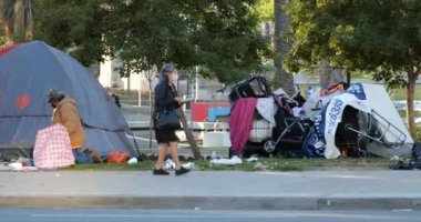 Los Angeles, CA USA - 27 Ocak 2021 MacArthur Park 'taki bir evsizler kampının önünden geçerken maske takan bir kadın
