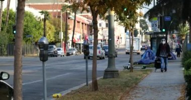 Los Angeles, CA USA - 29 Aralık 2020: Otobüs durağında yüz maskesi takmış bir kadınla yürüyen evsizler çadırı