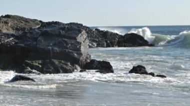 Büyük dalgalar Pasifik Okyanusu 'ndaki kayalık bir sahile süper yavaş çekimde çarpıyor.