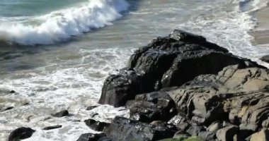 Dalgalar kıyıdaki kayalara çarpıyor, yüksek açı manzaralı.