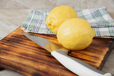 Bir mutfak bıçağıyla kesme tahtasındaki iki taze limon.