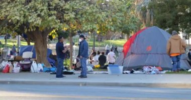 Los Angeles, CA USA - 31 Ocak 2021: MacArthur parkının kaldırımındaki çadırların önünden geçen yayalar ve evsizler