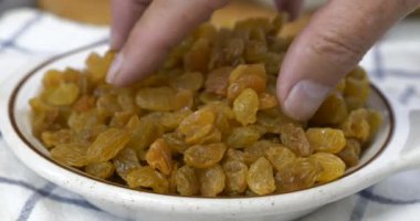 Parmaklar atıştırmalık kasesinden bir avuç dolusu altın kuru üzüm alıyor.