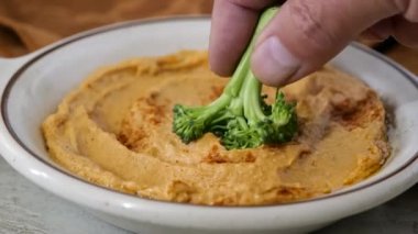 Bir brokoli çiçeğini humus kasesine batırmak süper ağır çekim.