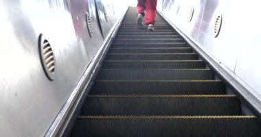 Kırmızı pantolonlu bir adamla metro istasyonundan yürüyen merdivene binmek.