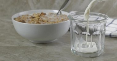 Bir kase tahıl gevreğinin yanında bardağa süt dökmek.