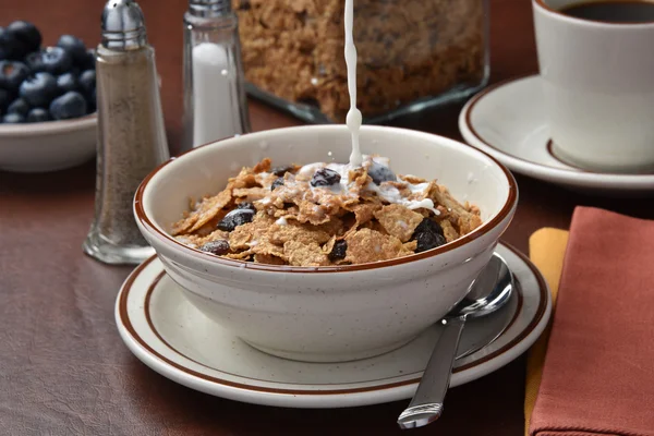 Pouring milk in bowl of flakes — Stock Photo, Image