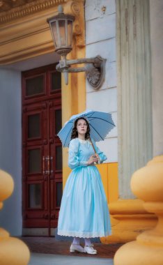 Malikanenin yanında şemsiyesi olan mavi elbiseli genç bir kadın.