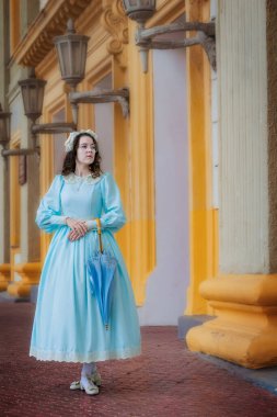 Malikanenin yanında şemsiyesi olan mavi elbiseli genç bir kadın.