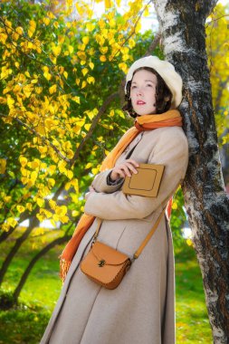 Bir sonbahar parkında elinde kitapla bir ağacın yanındaki kız..