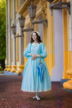 Köşkün yanında şemsiyesi olan mavi elbiseli bir kız.