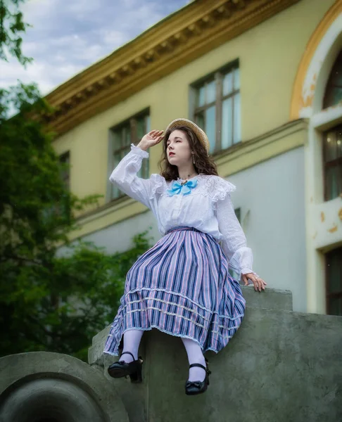 Woman in an vintage shirt and a long skirt sitting on terrace of mansion