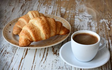 Tahta bir masanın üstünde bir fincan kahve ve kruvasan..