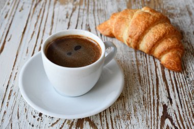 Tahta bir masanın üstünde bir fincan kahve ve kruvasan..