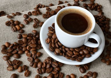 Bir fincan sıcak kahve ve bambu servis eden bir peçetenin üzerine kahve çekirdeği serpiştirmek..