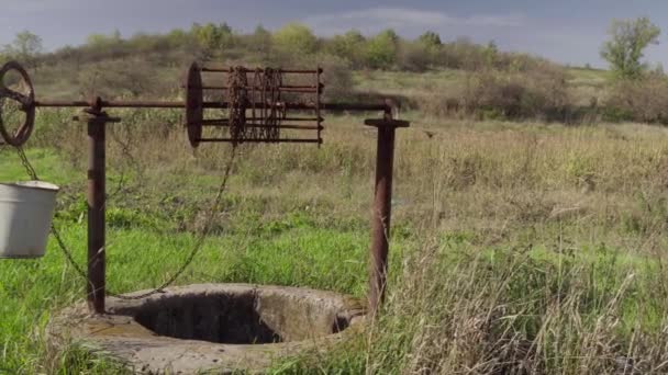 Un viejo pozo de agua en la granja rural. Un pozo abandonado en medio de hierba verde y árboles. — Vídeos de Stock