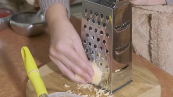 女の手が金属製のグラターにハードチーズをこすりつける チーズはまな板に滑らかに砕ける ホームキッチン — ストック動画