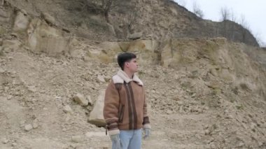 Kışlık ceketli bir adamın portresi bir dağın arka planına bakıyor.