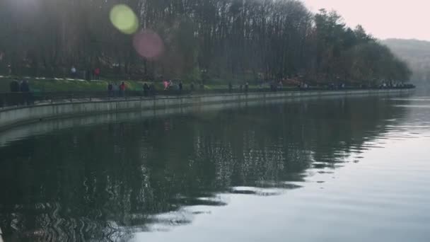 La gente camina en el parque al lado de un lago durante el día — Vídeos de Stock