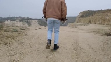Ceketli ve kot pantolonlu genç bir adam terk edilmiş bir taş taşıyıcısı boyunca yürüyor.