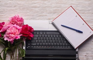 Açık dizüstü bilgisayarı, ofis malzemeleri, taze çiçekler, şık debriyaj çantası ve diğer aksesuarları beyaz bir masada, üst görünümde olan parlak kadınsı çalışma alanı.