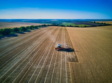 Hasat makinesindeki hava manzarası buğdayı gün batımında topluyor. Hasat zamanı, hasat zamanı. Kısmen hasat edilen tarladaki hasat makinesinin görüntüsü. Yaz, Moldova, Avrupa.