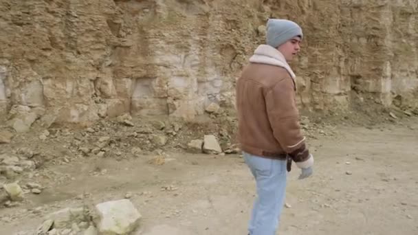 一个穿着夹克和牛仔裤的年轻人沿着一个废弃的石制加勒比人走着 — 图库视频影像