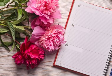 Kahvaltı için sabah kahve fincanı, boş defter, kalem ve pembe şakayık çiçekleri beyaz taş masanın üstünde düz bir şekilde duruyor..