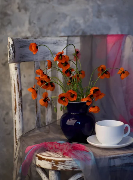 A Little Red Poppies Bouquet in blue vase on vintage chair. Poppies and cup of coffee.