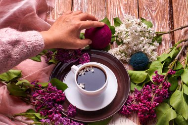Elinde bir fincan sabah kahvesi ile yukarıdan ahşap arka planda açan bahar leylak çiçekleri dalları var. Dümdüz yerde yatıyordu. Pahalı renkler. Çiçeklerin yaratıcı tasarımı.