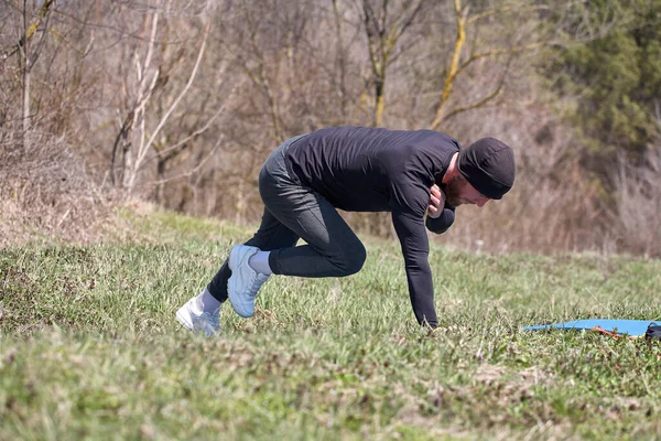 Hravý sportovec natahuje nohu za ním na fitness podložku v parku — Stock fotografie